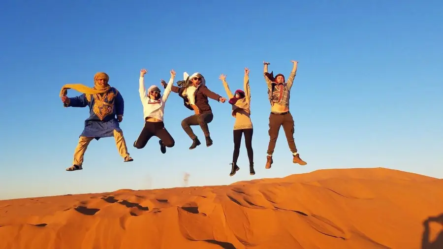 Travelers jumping on a Sahara dune with their Touareg guide